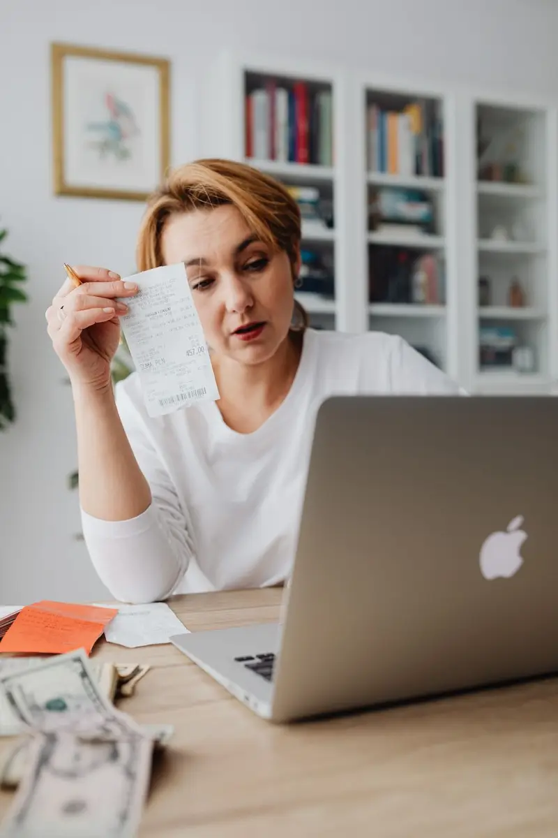 A woman going over a receipt and her budget on a laptop at home
