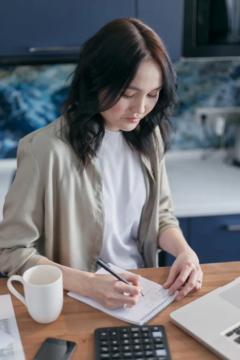 A woman calmly writing out a repayment plan at her kitchen table with a coffee
